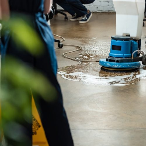 cropped view of cleaner washing floor with cleaning machine near colleagues