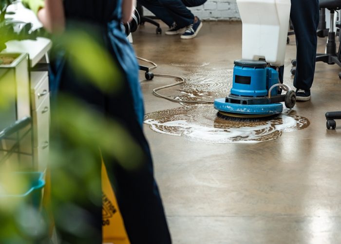 cropped view of cleaner washing floor with cleaning machine near colleagues